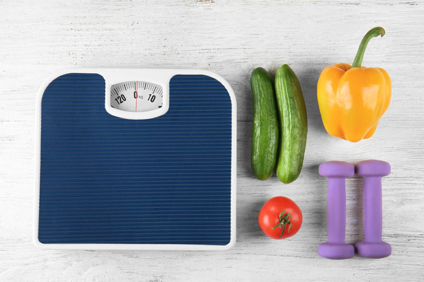 Fresh vegetables, dumbbells and scales on wooden background. Healthy food concept - Photo, Image