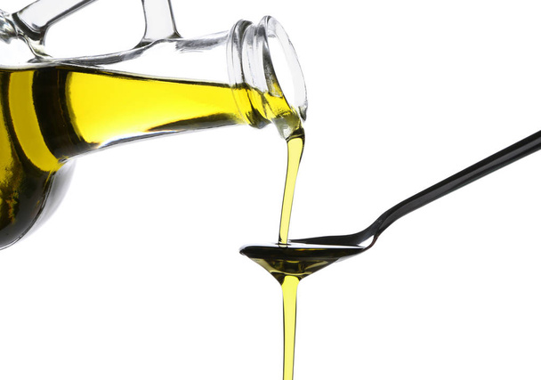 Pouring of olive oil from glass jug into spoon on white background - Foto, Imagem