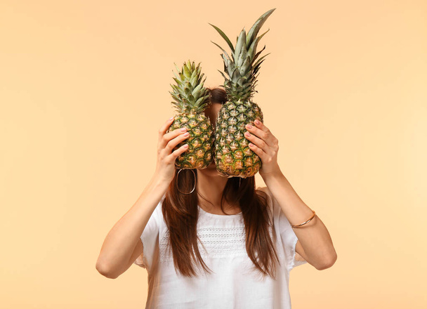 Young woman hiding face behind two pineapples on color background - Photo, Image