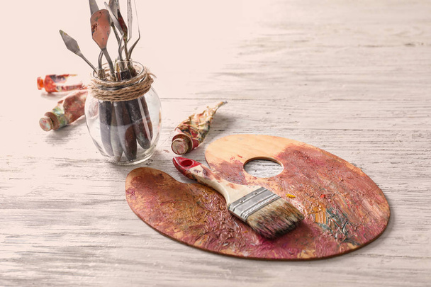 Paleta de pintura con pincel y cuchillos en tarro sobre mesa
 - Foto, imagen