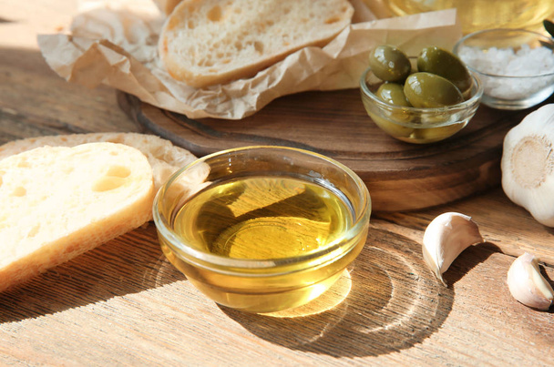 Olive oil with fresh bread and garlic on wooden table - Zdjęcie, obraz