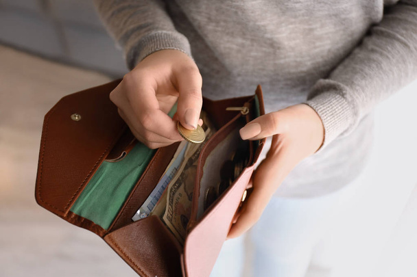 Young woman putting coin into wallet indoors, closeup. Money savings concept - Фото, зображення