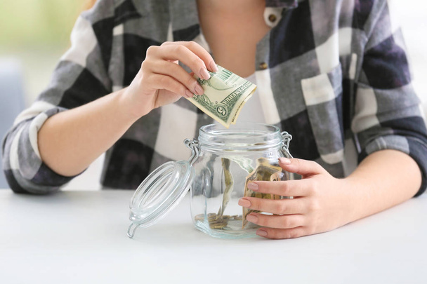 Молода жінка кладе банкноту долара в скляну банку, крупним планом. Концепція заощадження грошей
 - Фото, зображення