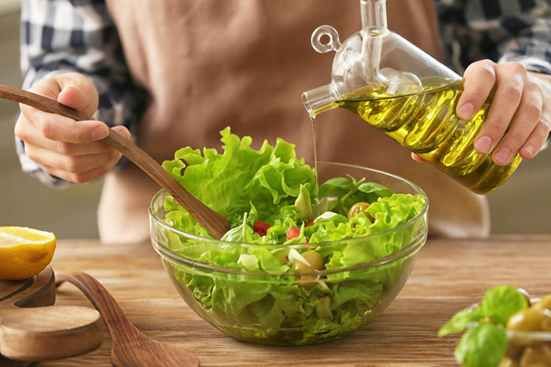 Woman adding olive oil into bowl with fresh vegetable salad on table - Fotografie, Obrázek