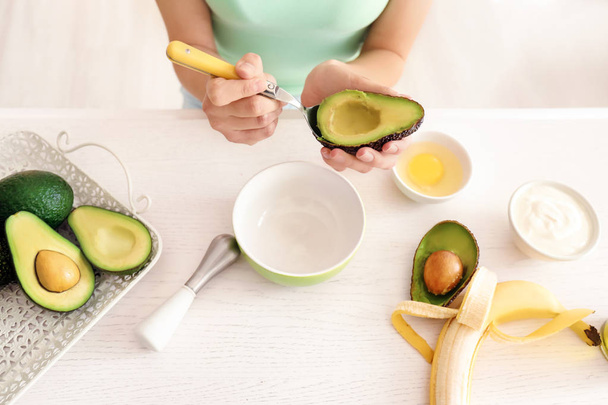 Woman making nourishing mask with avocado in kitchen - Photo, Image