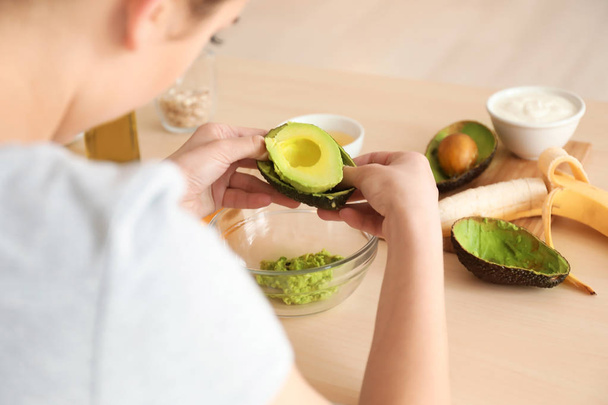 Woman making nourishing mask with avocado in kitchen - Foto, afbeelding
