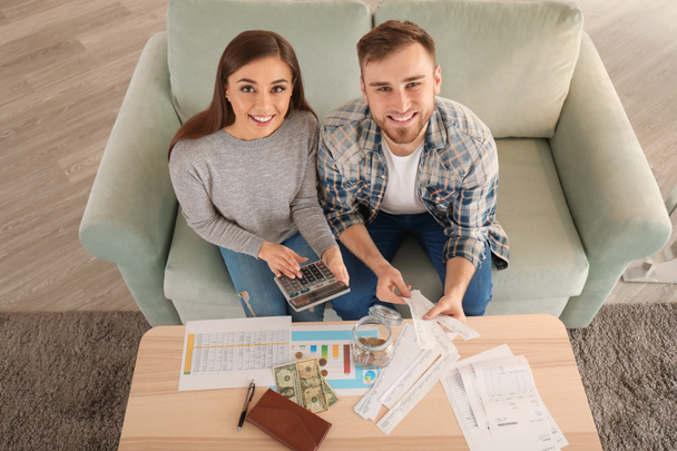 Happy couple with pay bills, calculator and money counting expenses indoors. Money savings concept - Photo, Image
