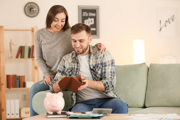Happy wife near husband with salary indoors. Money savings concept - Valokuva, kuva