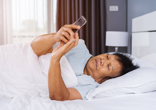 senior woman using mobile phone on a bed - Valokuva, kuva