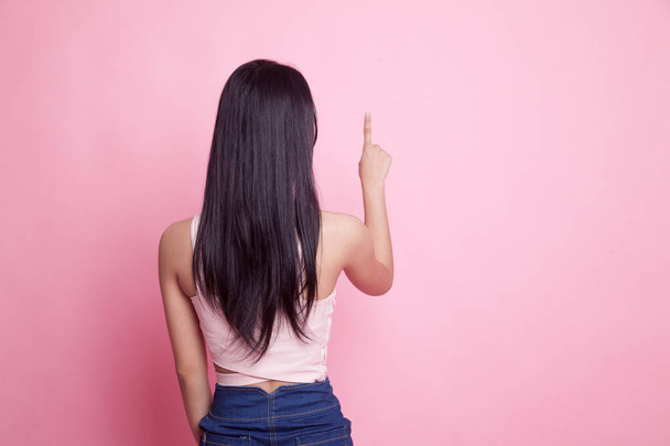 Back of Asian woman touching the screen with her finger on pink background - Foto, afbeelding