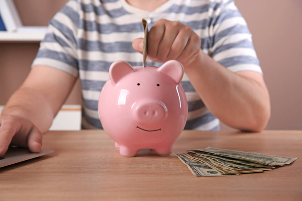 Ο άνθρωπος τοποθέτηση χρημάτων σε Τράπεζα piggy σε πίνακα - Φωτογραφία, εικόνα