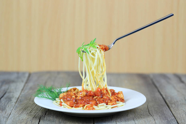 Špagety s rajčatovou omáčkou na stříbrné lžičky plovoucích v bílé misce na dřevěnou podlahu, pojem jíst dobré jídlo je zdravotní péče. - Fotografie, Obrázek