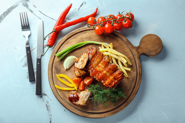 Placa de madeira com deliciosas costelas grelhadas, legumes e batatas fritas na mesa
 - Foto, Imagem