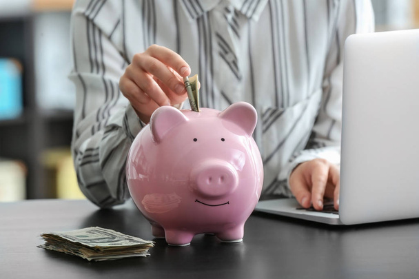 Uma mulher a investir dinheiro no Piggy Bank. Conceito de poupança
 - Foto, Imagem
