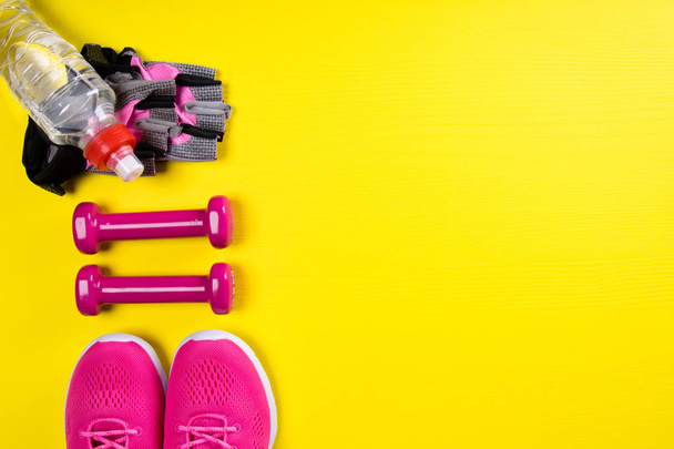 pink items for fitness and a bottle of water, on a yellow background, with a place for writing - 写真・画像