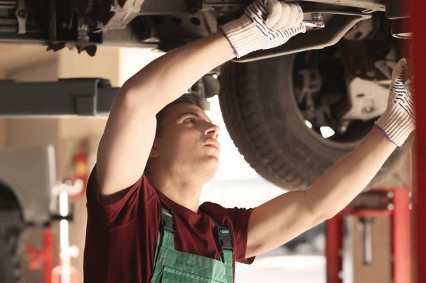 Young auto mechanic repairing car in service center - Foto, imagen
