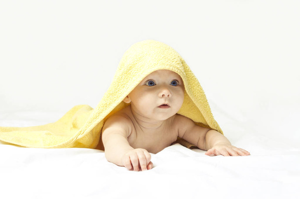 Charmante, mignonne, heureuse petite fille aux yeux bleus dans une serviette jaune sur fond blanc. - Photo, image