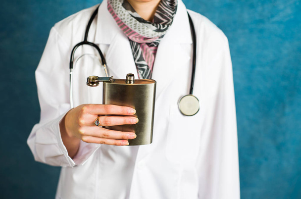 Женщина-врач держит фляжку рядом с бедром.
 - Фото, изображение