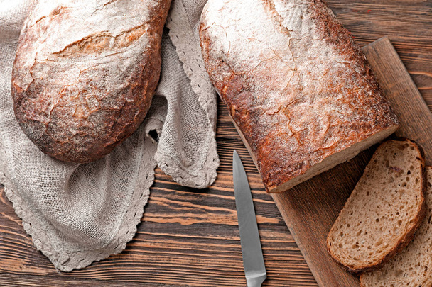 Knife and board with cut fresh tasty bread on wooden table - Foto, imagen