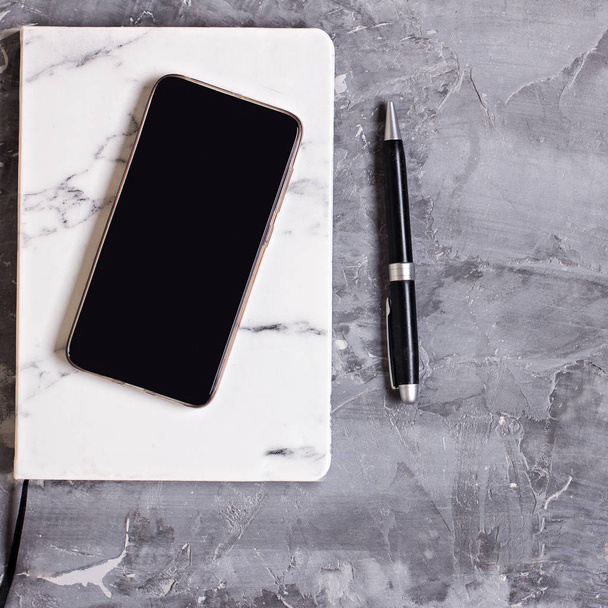 Bloc de notas, teléfono móvil, pluma sobre un fondo de cemento gris. Concepto empresarial
. - Foto, imagen