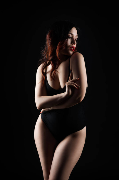 Beautiful sexy woman in bodysuit posing on black studio background, perfect female body, low key studio shot - Zdjęcie, obraz