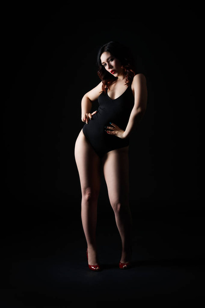 Beautiful sexy woman in bodysuit posing on black studio background, perfect female body, low key studio shot - Zdjęcie, obraz