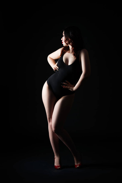 Beautiful sexy woman in bodysuit posing on black studio background, perfect female body, low key studio shot - Фото, изображение