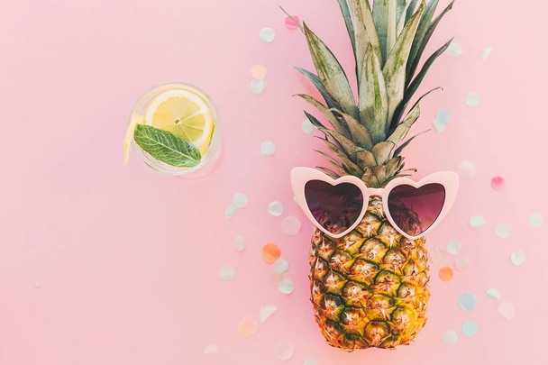 summer vacation and party concept. stylish pineapple in pink sunglasses and cocktail drink on trendy pink paper background with confetti. flat lay. space for text. summer travel and holidays - Photo, Image