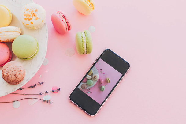modern food photography concept. phone with photo of stylish colorful macaroons in vintage plate on trendy pink paper with lavender. space for text. instagram blogging concept - Photo, image