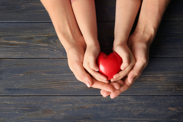 Τα χέρια της μητέρας και του παιδιού που κατέχουν κόκκινη καρδιά σε ξύλινο πλαίσιο - Φωτογραφία, εικόνα
