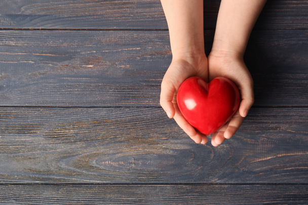 Руки дитини з червоним серцем на дерев'яному фоні
 - Фото, зображення