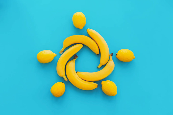 gele bananen in cirkel met citroenen op blauw papier trendy achtergrond, plat leggen. lichte zomer plat lag concept. sappige abstracte achtergrond, pop-art stijl. moderne afbeelding van zon - Foto, afbeelding