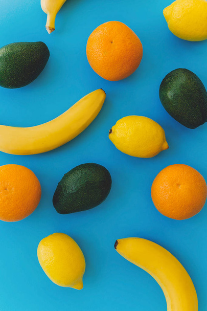 Bananen, Orangen, Zitronen, Avocado auf blauem, trendigem Papierhintergrund lagen flach. Sommer Multi-Frucht-Konzept, buntes Muster. Gesunder Lebensstil und Urlaubsstimmung. - Foto, Bild