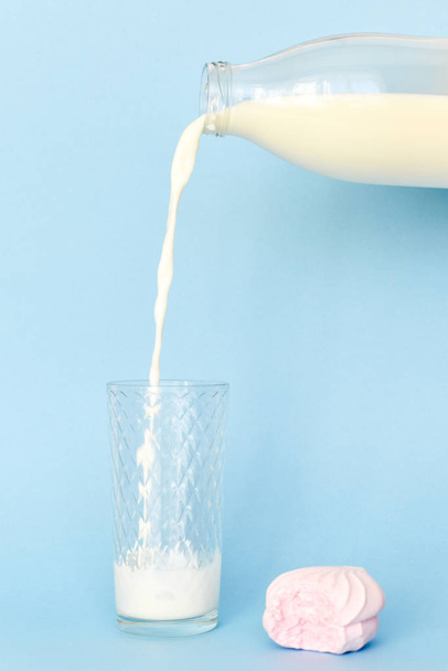 Из прозрачной стеклянной бутылки наливайте молоко в стакан. Синий фон
 - Фото, изображение