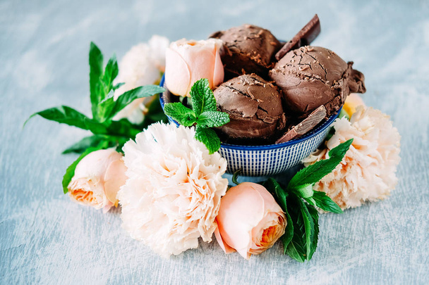 Drie bollen donkere chocolade-ijs sundae met zoete bloemen smaak omgeven door rozen, anjers en muntblaadjes - Foto, afbeelding