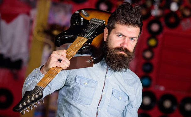 Rock musician concept. Musician with beard play electric guitar. Talented musician, soloist, singer carries guitar in music club on background. Man on calm face carrying guitar on shoulder - Photo, Image