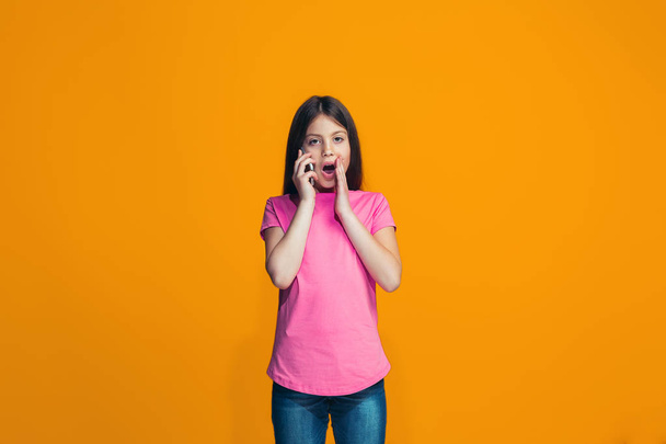 The happy teen girl standing and smiling against orange background. - Photo, Image