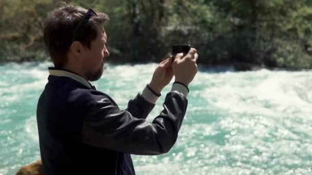 um jovem segurando um smartphone e fotografando o leito do rio no verão
 - Filmagem, Vídeo