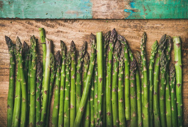 Seasonal harvest produce . Raw uncooked green asparagus in row over rustic wooden background - Foto, Bild