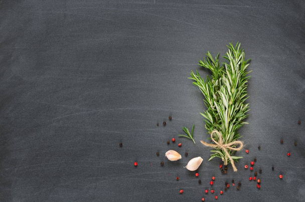 Bunch of rosemary with garlic and spices on chalk board. Copy space composition. Overhead shots. Vignette - Фото, изображение