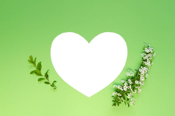 Paper heart with branches of flowers on green background. Overhead shots. Flat lay. Copy space background - Fotó, kép