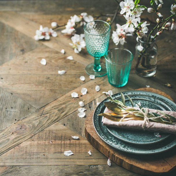 Spring Easter holiday Table setting. Tender almond blossom flowers on branches, plates, glasses and cutlery over vintage wooden table - Fotografie, Obrázek