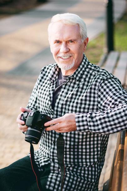 Experience more. Jolly mature man utilizing camera and resting on bench - Foto, imagen