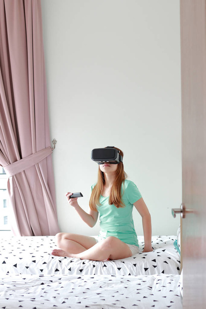 Young woman wearing virtual reality glasses at home. A virtual reality headset is a head-mounted device that provides virtual reality for the wearer. - Foto, afbeelding