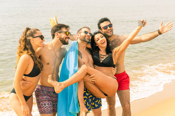 Happy friends taking a selfie on the beach in Barcelona. Multiracial group of best friends enjoying summer time together ready to take a swim. Happiness and friendship during a travel in Spain - 写真・画像