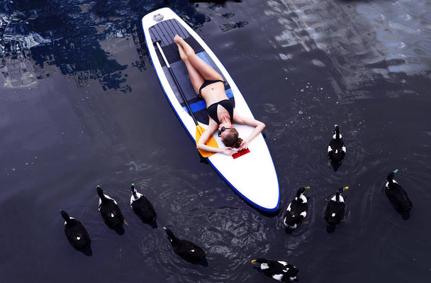 SUP Встань на подставку женщина посадка на озере, стоя счастливой на подставке на голубой воде
. - Фото, изображение