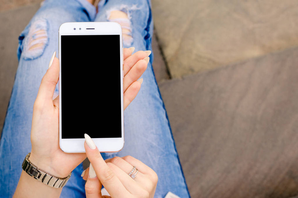 Close Up branco Smartphone celular segurando em mãos de mulher elegante rasgado Jeans unhas compridas Denim preto Oled Display Stone fundo
 - Foto, Imagem