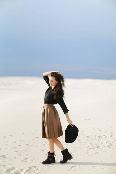 kaukasische stilvolle Fotomodell steht auf Schnee und trägt Rock und schwarze Bluse. Hut auf. - Foto, Bild