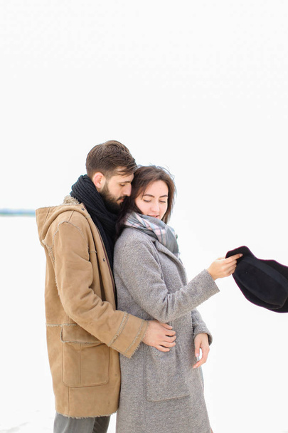 Giovane uomo che abbraccia donna indossando cappotto grigio e sciarpa in bianco sfondo invernale
. - Foto, immagini