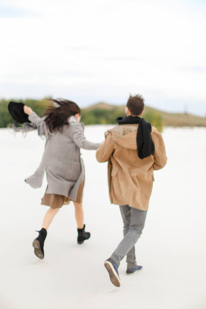 Young stylish couple walking on snow and holding hands, winter background. - 写真・画像
